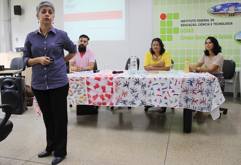 A palestra que tratou das especificidades da EJA nos institutos federais foi proferida pela professora Maria Margarida Machado (UFG), em pé, e pela professora Mad'Ana Ribeiro de Castro (IFG), ao centro da mesa com os coordenadores dos cursos técnicos em Alimentos e em Modelagem do Vestuário, respectivamente professores Sandro Henrique Ribeiro e Yane Ondina de Almeida